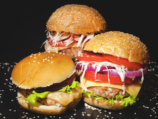Fast food concept: juicy homemade big burgers with cheese and vegetables on a dark background  