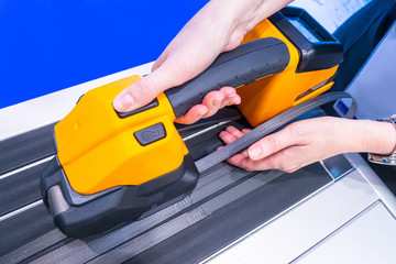 Hand tool for packing boxes with plastic tape. Strapping machine close-up. The girl packs the box....