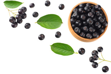 Chokeberry in wooden bowl with green leaves isolated on white background. Black aronia. Top view.