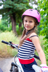 Fototapeta na wymiar Little cute girl in a pink helmet near a bicycle