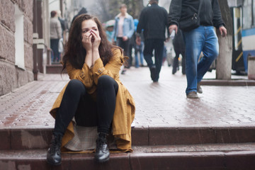 Sad young woman sitting outdoors in autumn on a rainy day.