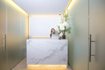 Front view of a modern reception and beautiful woman receptionist answering the phone.