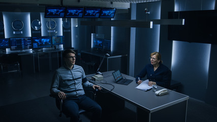 Female Special Agent Conducts Lie Detector / Polygraph Test on a Young Suspect. Expert Examiner Questions Accused in Interrogation Room. Laptop Records Reactions. High Angle Retreating Shot.