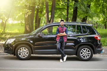 Young handsome indian man standing near his car on the road