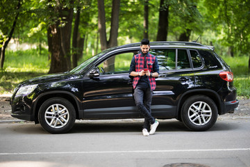 Inviting friend for a journey. Handsome young man use the mobile phone and smiling while leaning at his car © F8  \ Suport Ukraine