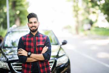 Young indian man standing near his car.