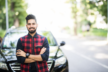Young indian man standing near his car.