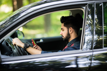 Indian man drive car while hand holding smartphone to use online application.
