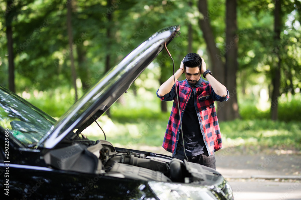 Wall mural closeup portrait, young indian man having trouble with his broken auto, opening hood trying to fix e