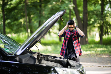 Closeup portrait, young indian man having trouble with his broken auto, opening hood trying to fix...