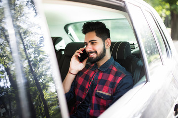 Casual indian man talk on mobile phone in rear of the car