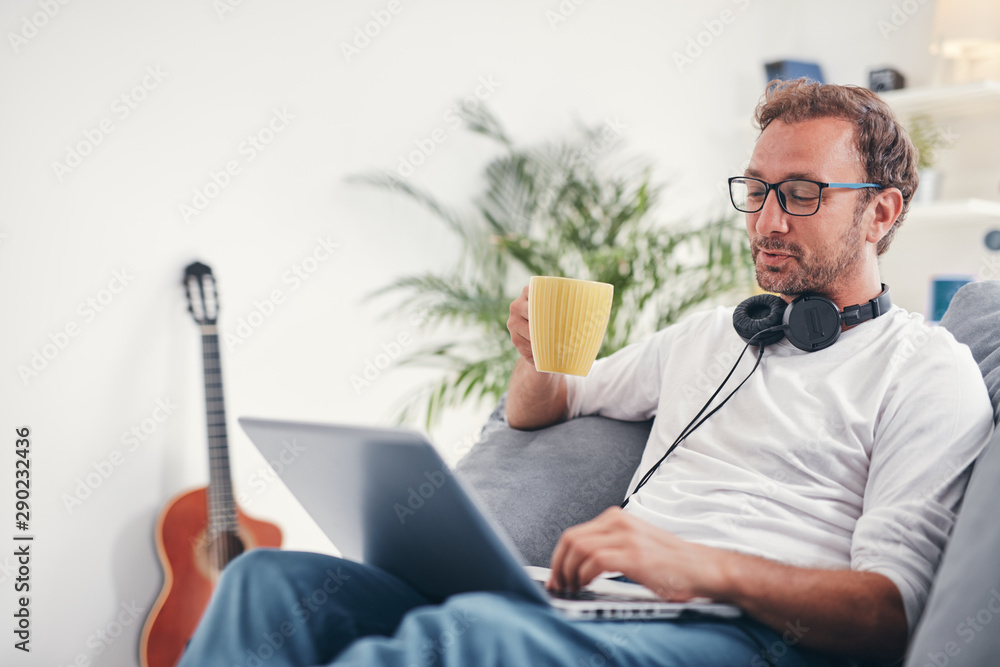 Wall mural Man listening to music and using laptop in the living room.