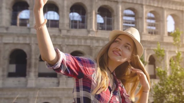 Young blonde woman with blue eyes and long hair, taking selfie with smartphone at Colosseum, Rome.