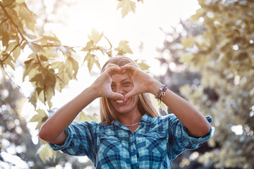 Young woman outdoors making heart - shape symbol for love and romance.