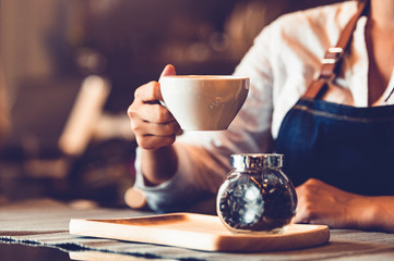 Closeup of professional female barista hand making and holding white cup of coffee. Happy young...