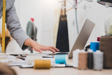 Closeup of female fashion designer hand working in clothing shop studio and using laptop computer...