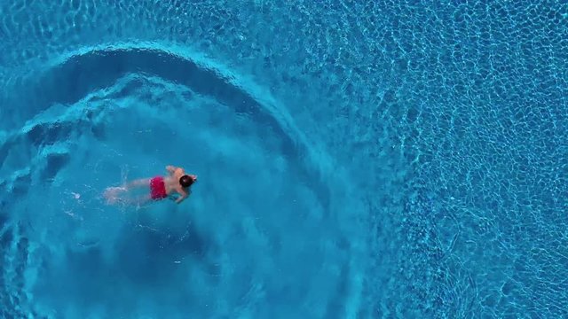 View from the top as a man dives into the pool like a bomb and swims under the water