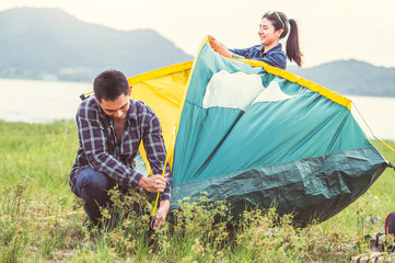 Two Asian couples prepare pitch camping tent to stay outdoors meadow overnight for honeymoon camping picnic. People lifestyle and Valentine day love concept. Nature travel vacation relaxation activity