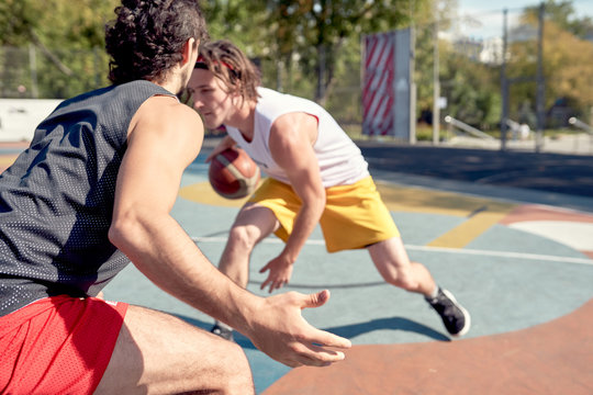 Photo of young sports men playing basketball on playground on summer day.