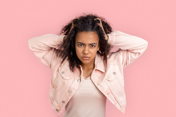 Freestyle. African girl in denim jacket standing isolated on pink messing hair looking camera angry...