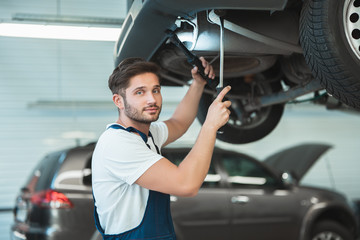 young handsome mechanic working in car service department fixing the problem in vehicle chassis