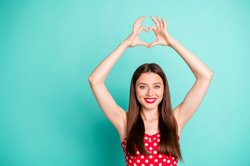Fototapeta na wymiar Portrait of cute lady smiling showing heart shaped sign wearing polka dot dress skirt isolated over teal turquoise background