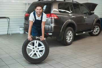 Fototapeta na wymiar young handsome mechanic working in car service department fixing flat tire looks pleased