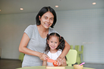 Fototapeta premium Portraits Asian mother and daughter slicing vegetable on chopping board at play room. Mother teaches her little child girl to cooking.
