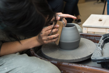 Fototapeta na wymiar The master creates products from gray clay on a potter's wheel. Girl creates a ceramic vase