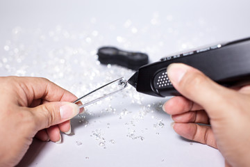 Diamonds in front of a white background, reflections on the ground. brilliant cut diamond held by right hand, diamond testing machine, tester, white gemstone, diamond checking equipment.