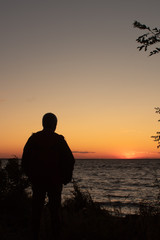 Silhouette of a man on the seashore in the rays of the setting sun