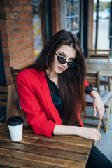 Young beautiful brunette girl, office clothing style, sitting on the street at a table in a cafe, street model posing style, makes notes in a notebook, talking on the phone