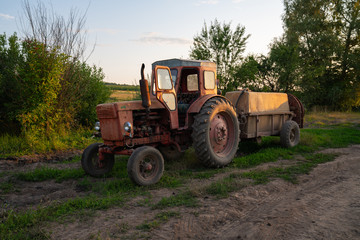 Old red tractor with a tank, barrel sprayer standing near a dirt road