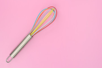 close up of colorful kitchen whisk on pink background