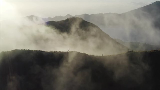 Aerial view of volcanos and light fog rising up from the ground. Silhouettes of tourists hiking in mountains. Bali island, Indonesia