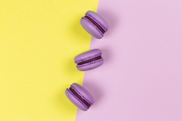 Three purple french macarons on a yellow and purple background.