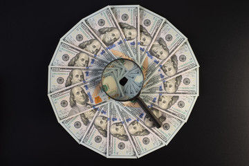 Fototapeta na wymiar A pile of one hundred dollar bills laid out in a circle. In the middle of a magnifier, on a black background