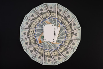 A pile of one hundred dollar bills laid out in a circle. In the middle of playing cards, on a black background