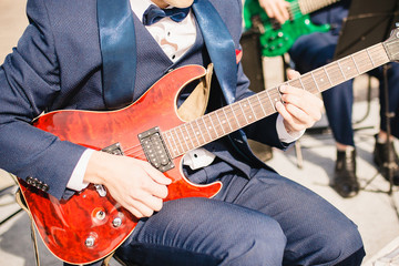 Musician orchestra guitarist in a blue suit with a bow tie and with a red electric guitar during a concert close-up