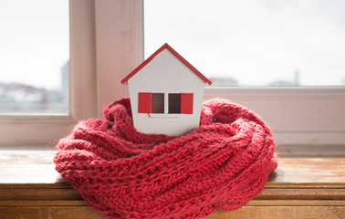 house in winter - heating system concept and cold snowy weather with model of a house wearing a knitted cap
