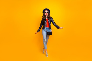 Full body photo of cute pretty girl walking with her friends on spring holidays wear modern black leather jacket denim jeans isolated over yellow color background