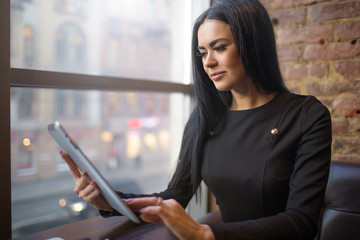 Woman successful government worker checking e-mail on portable touch pad computer, sitting in restaurant after work day. Confident female lawyer using application on digital tablet during rest in cafe