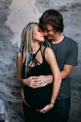 Pregnant woman with husband standing together indoors and hugging