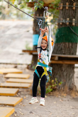 Little girl in helmet climbs ropes in adventure park outdoors. Extreme sport, active leisure on nature.
