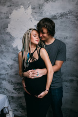 Smiling pregnant young couple hugging while standing together at home