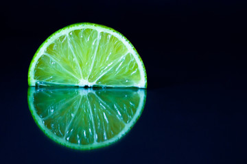 Lime slice on black reflective background. Creative food concept, minimal style.