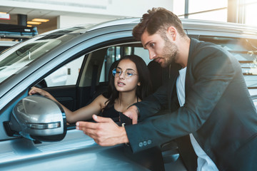 Fototapeta na wymiar handsome man manager consulting young beautiful woman client while choosing new car in dealership center