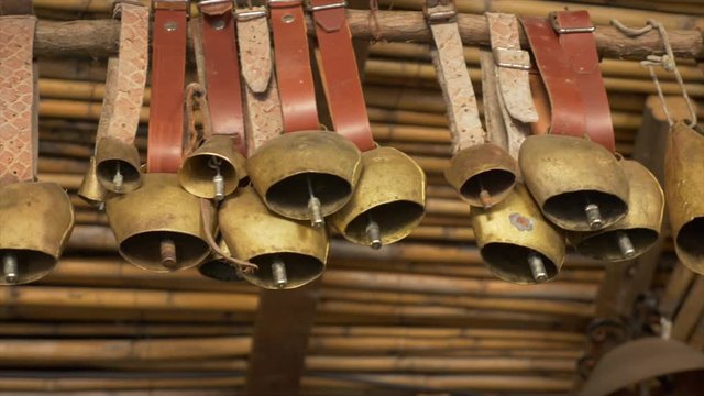 Pan shot over old ship bells hangingd from a wooden cane roof.
