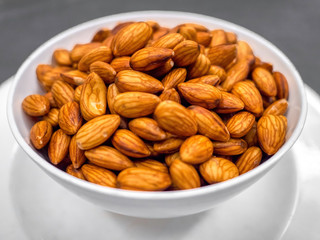 Closeup fresh almonds in white bowl on dark table background, Fresh almonds are material for almonds milk.