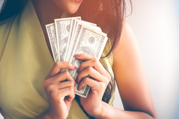Close up of a business woman with black hair, long hair, wearing a yellow shirt. She holds a 100 dollar banknote in a lot of hands, the concept of a successful business.